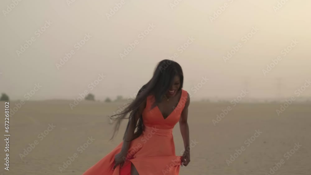Swarthy young woman with long hair walking barefoot on desert sand in a dress developing in the wind
