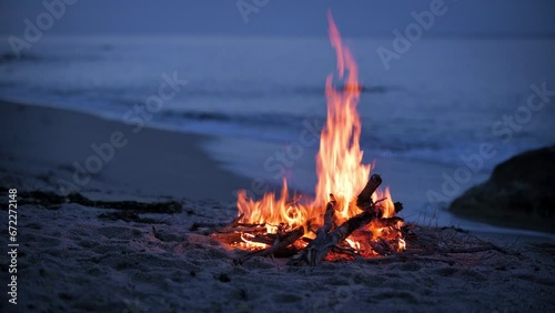 A campfire burns on a deserted sandy beach at the seashore in the evening