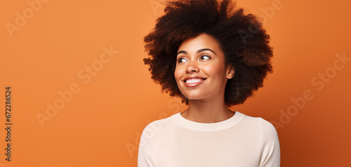 Joyful Beautiful African American Woman with Voluminous Afro Hair, Upward Gaze on a Warm Orange Background. Soft and Perfekt Skin, Perfect White Teeth.