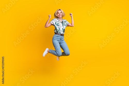 Full length photo of overjoyed lucky cute girl dressed print shirt win bet clenching fists jumping isolated on yellow color background