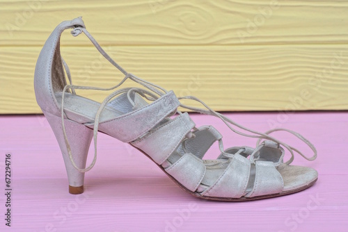 one white womens leather high heel sandal stands on a pink wooden table against a yellow wall