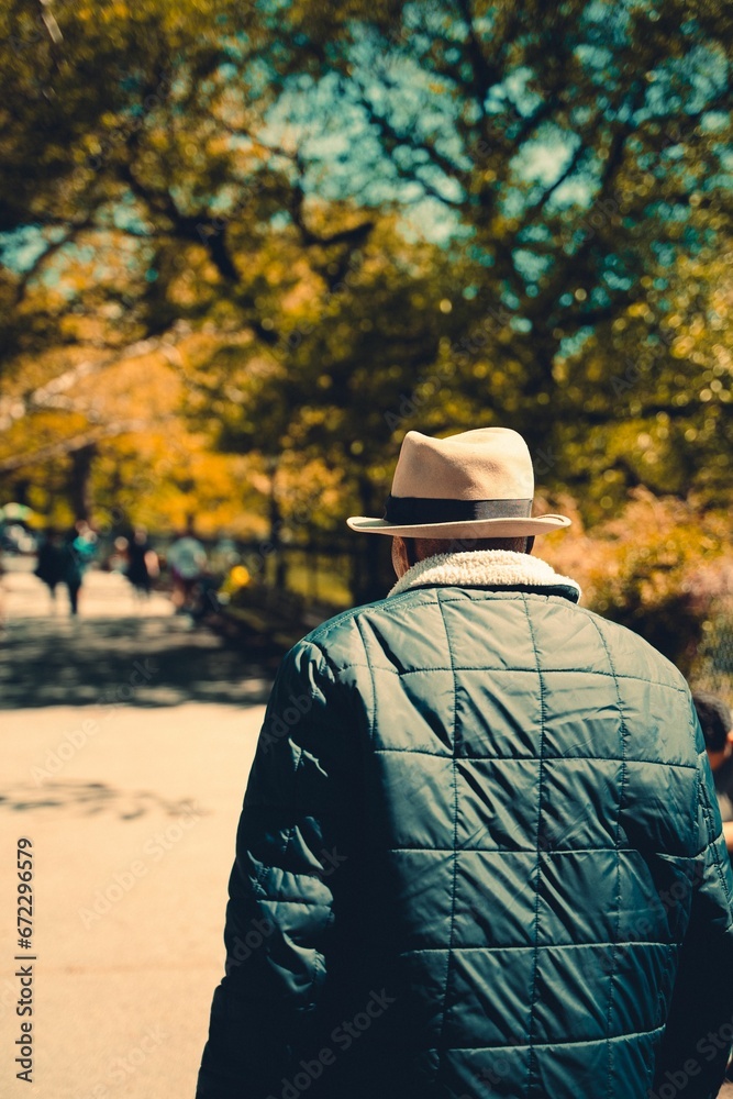 Shallow focus of an adult man with a fedora hat walking in a park in autumn