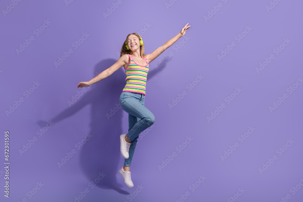 Full length photo of lovely teen blonde lady jumping dance listen music wear trendy striped garment isolated on purple color background