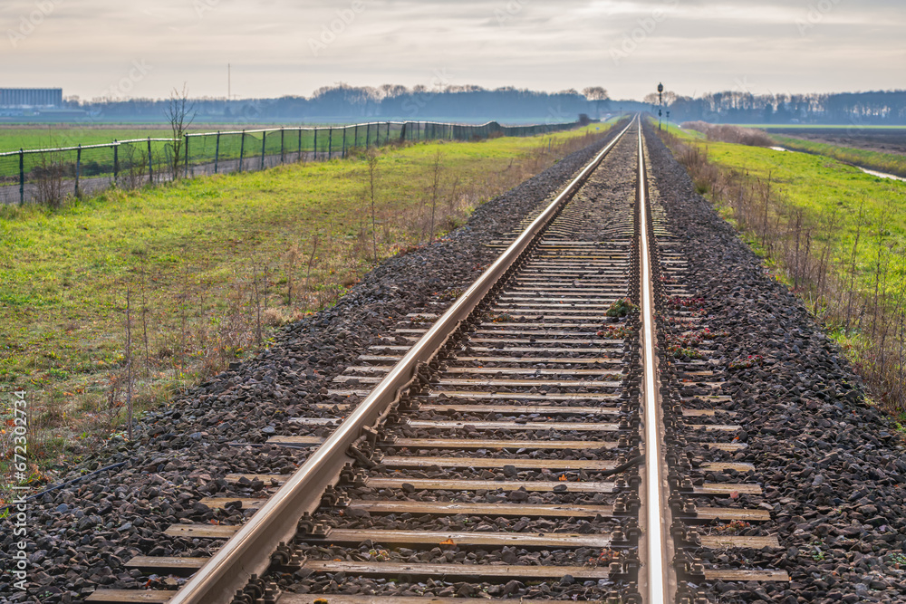 Fototapeta premium Single track rails in a rural area. The rails are mounted on wooden sleepers in a ballast bed of coarse crushed stone. It is a dark day at the start of the Dutch winter season.