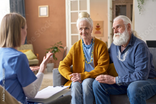 Senior couple sitting on sofa and talking to social worker during her visit to home photo
