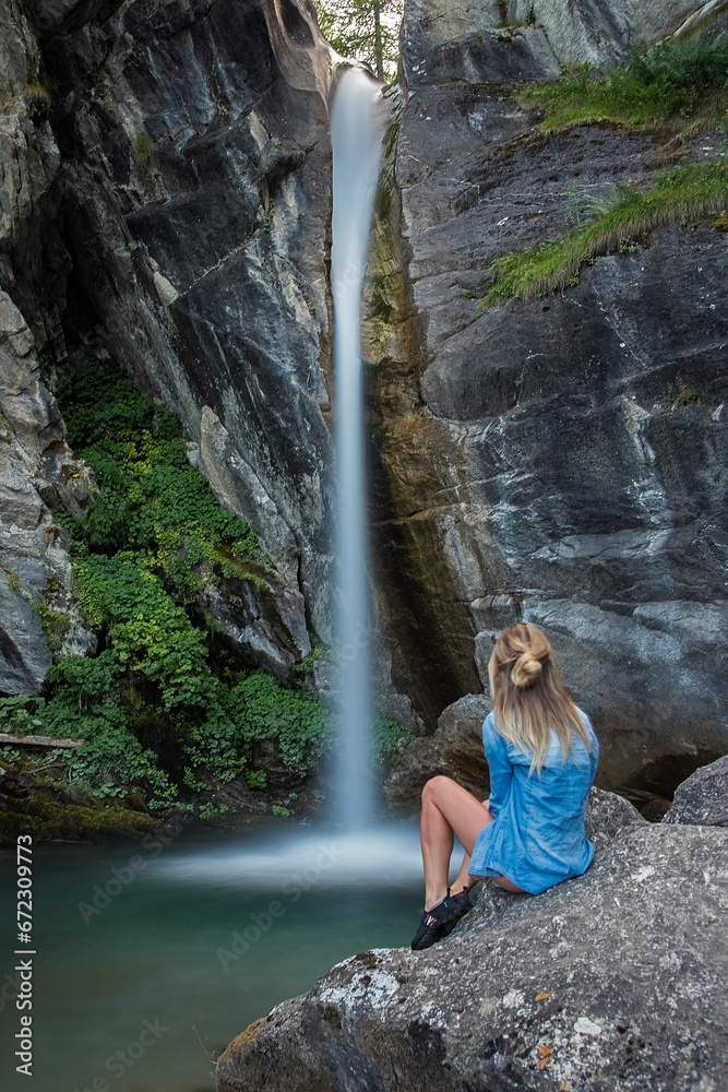 Model shot from behind posing on a stone with a silk effect waterfall in the background. Spa and relaxation concept.