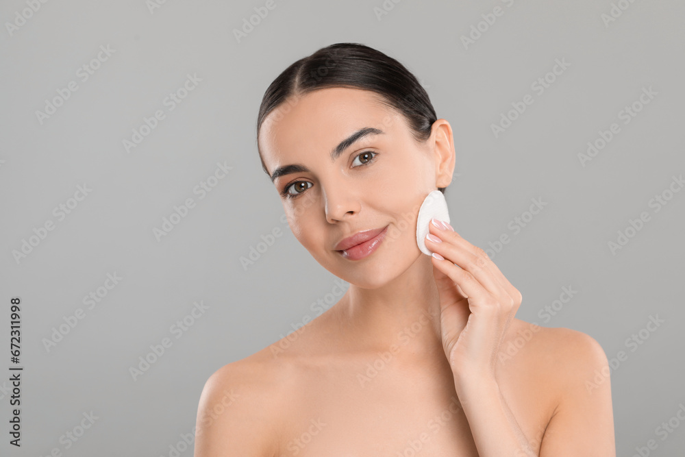 Beautiful woman removing makeup with cotton pad on light grey background, space for text Beautiful woman removing makeup with cotton pad on light grey background, space for text