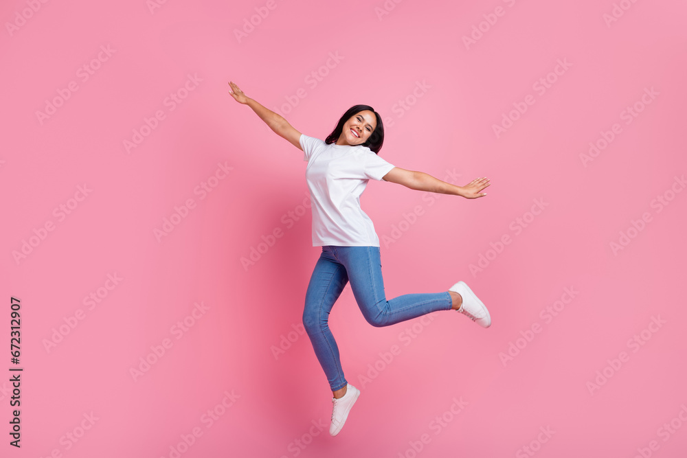 Full body size photo of carefree young woman flying jump trampoline wings arms enjoying traveling isolated on pink color background