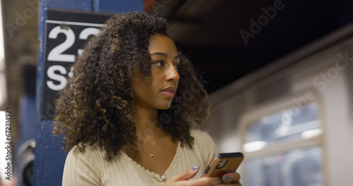 Young black woman using smartphone at a subway platform