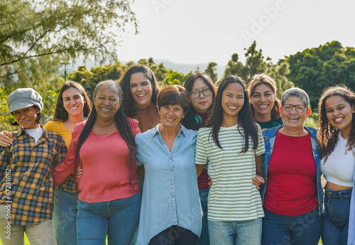 Group of multi generational women hugging each other while smiling on camera at city park - Multiracial female friends and community concept