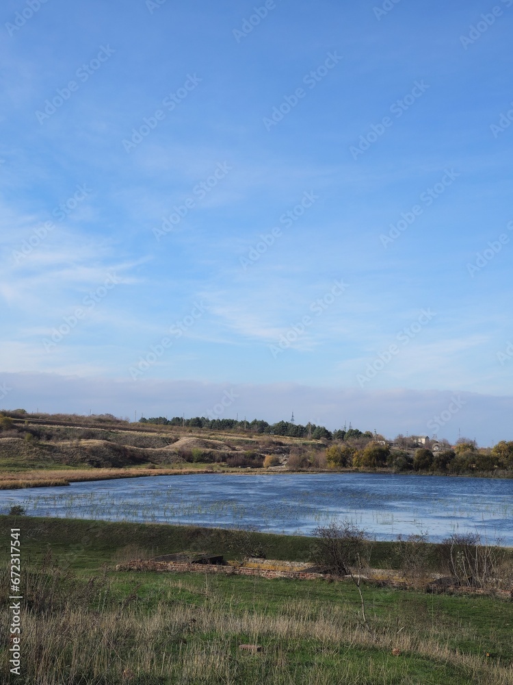 A field with a body of water and a blue sky with clouds