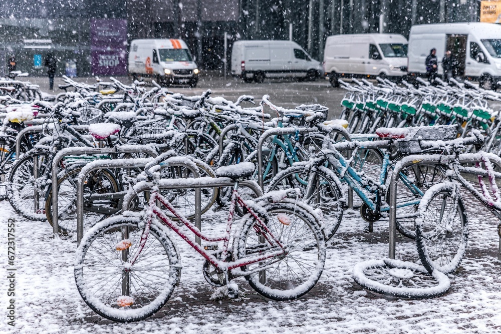 Row of bicycles, parked in front of a building, are covered in a layer of snow