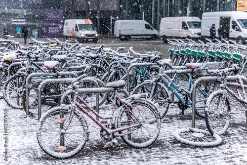 Row of bicycles, parked in front of a building, are covered in a layer of snow