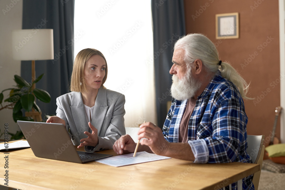 Insurance agent talking to senior man while they sitting at table with laptop at home