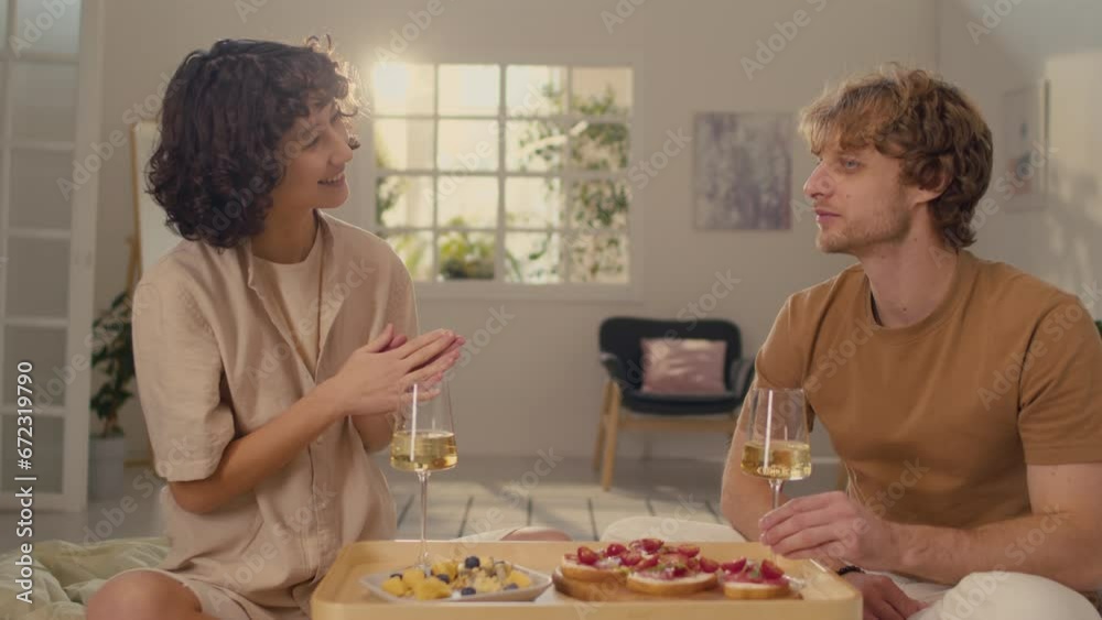 Medium shot of young couple sitting at home feeding each other while celebrating their anniversary