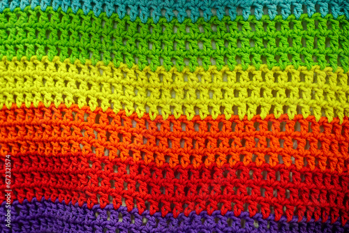 A knitted wool fabric in the colors of the rainbow.Crochet, handmade, needlework. Multicolored skein of threads. Sweater structure.Horizontal stripe.