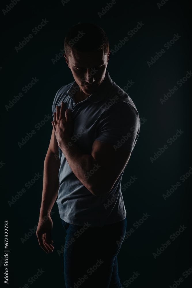 Naklejka premium Appealing and well-built man standing in a dark room and flexing his muscles