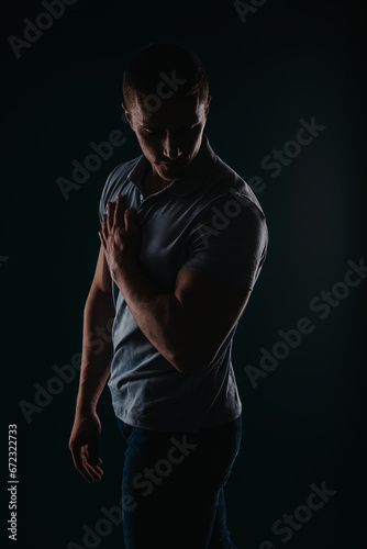 Appealing and well-built man standing in a dark room and flexing his muscles