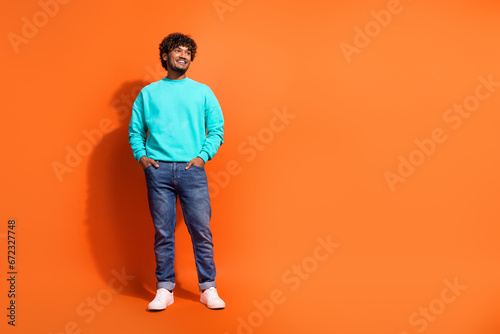 Full body portrait of cheerful creative person put arms pockets look empty space isolated on orange color background