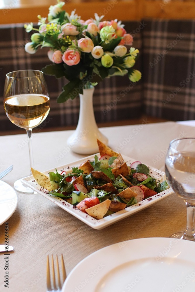 Bowl of Fattoush salad, with a variety of colorful ingredients and a glass of wine in a restaurant