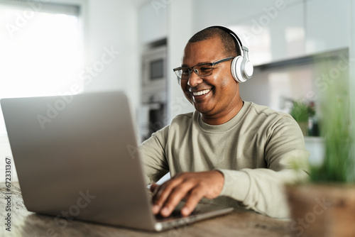 Happy mature Latin man using laptop at home - Technology and smart working concept photo