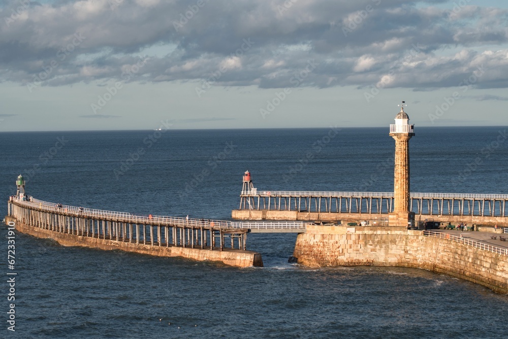bridge spanning a body of water, leading to a coastline with Whitby Lighthouse in Yorkshire England