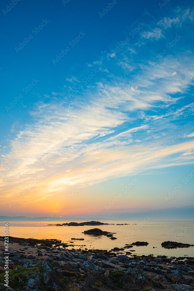 Dawn breaking over the Isle of Arran with a coastal cloudscape over Ardnacross Bay viewed from a rocky beach near Peninver on the Kintyre Peninsula, Argyll & Bute, Scotland UK Dawn breaking over the Isle of Arran with a coastal cloudscape over Ardnacross Bay viewed from a rocky beach near Peninver on the Kintyre Peninsula, Argyll & Bute, Scotland UK