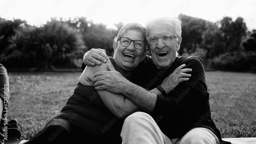 Happy senior couple having fun smiling in Park City. Older people enjoy together outdoors in nature. Black and white editing - obrazy, fototapety, plakaty 