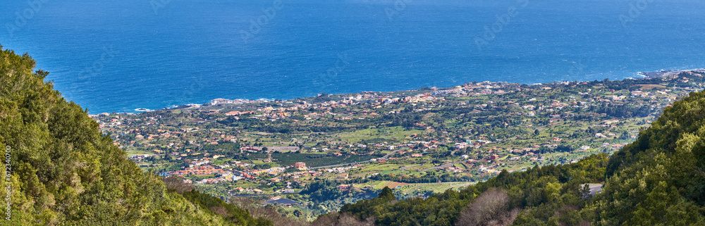 Landscape of a coastal city between hills and mountains from above. A peaceful village beside calm blue ocean water in the Canary Islands. High angle view of Los Llanos, La Palma in summer