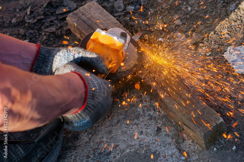 Bright sparks of metal fly from the disk of an angle grinder. A power tool in the hands of a worker is used to cut metal parts. photo