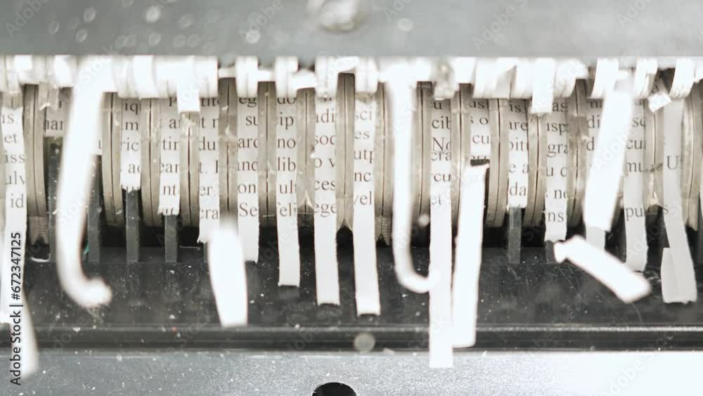 Teeth of the shredder rotating and destroying paper lorem ipsum text. Paper shredder machine used to cut secret documents with sensitive information, confidential, personal financial information.