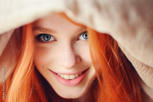 Young, blue-eyed redhead woman under the duvet, smiling.