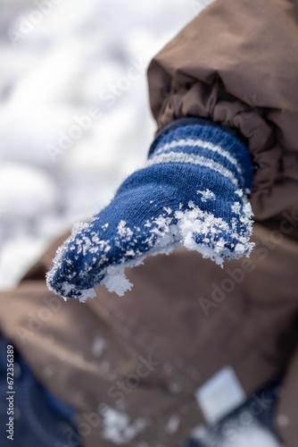 Vertical shot of a kid wearing a blue glove covered in the snow in a park