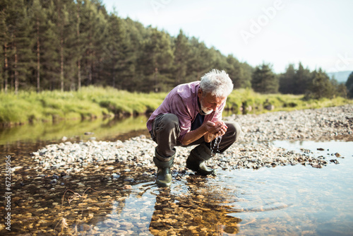 Senior man cleaning hands with fresh water in nature