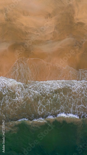 Vertical shot of powerful ocean waves crashing onto the sandy beach