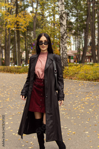 Young woman in black sunglasses and leather raincoat. Natural. Attractive woman in park