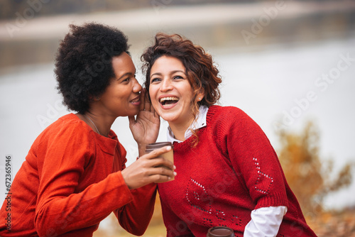 Two happy female friend talking and sharing life stories, enjoying autumn outdoors , drinks coffee. Women's friendship