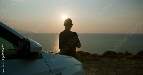 Young man standing on the edge of a cliff seashore enjoying beautiful seascape with sunset photo