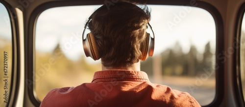 A Caucasian male in his youth sits in a car seat with headphones on engaging in guided meditation for relaxation while also potentially enjoying music or podcasts by real people From behind 