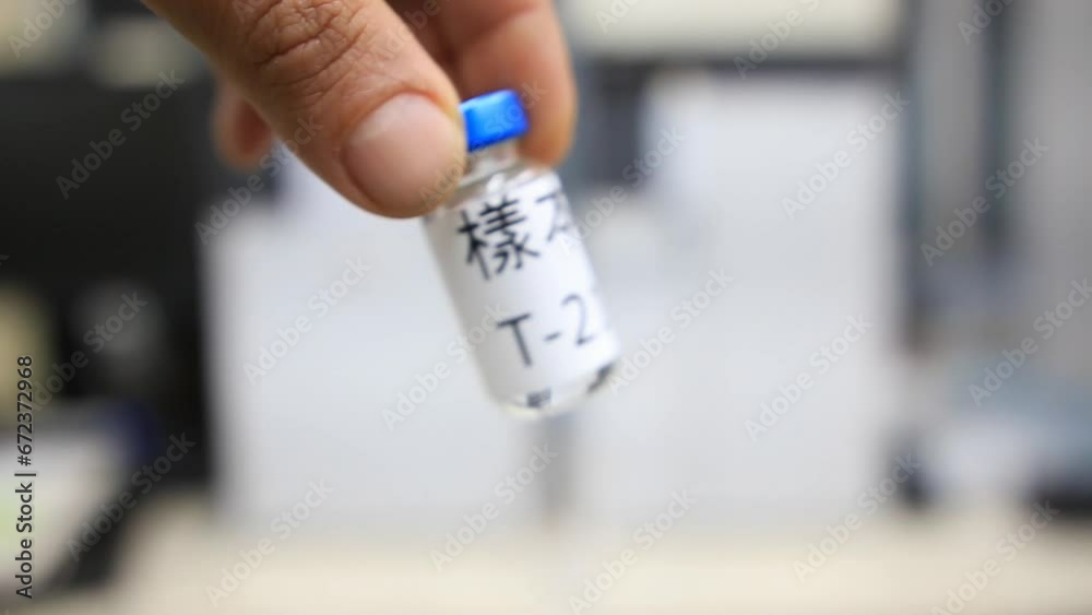 A close up from a man holding a vial with a liquid labelled as sample in Chinese characters inside a analytical chemistry laboratory A close up from a man holding a vial with a liquid labelled as sample in Chinese characters inside a analytical chemistry laboratory
