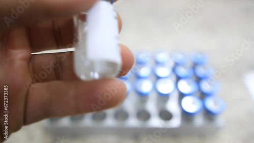 A close up from a man picking up a vial with a liquid labelled as sample in hindi inside a analytical chemistry laboratory photo