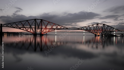 Aerial view of the Forth Bridge, spanning a river and illuminated with red lights at night