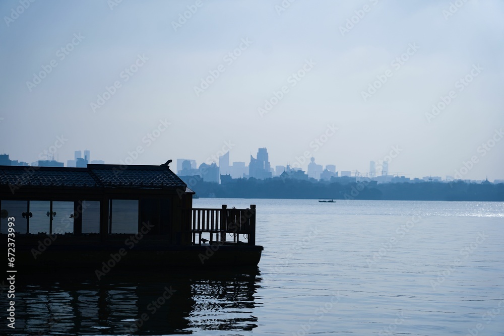 Closeup of a craft floating on a tranquil body of water, with a backdrop of urban structures Closeup of a craft floating on a tranquil body of water, with a backdrop of urban structures