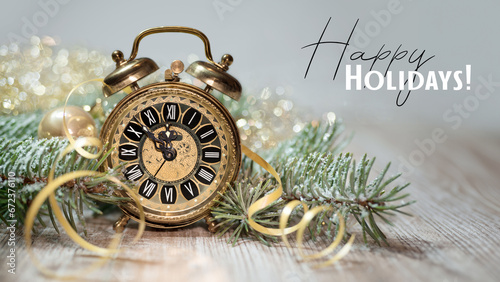 Old golden alarm clock showing five to midnight. Text Happy Holidays.