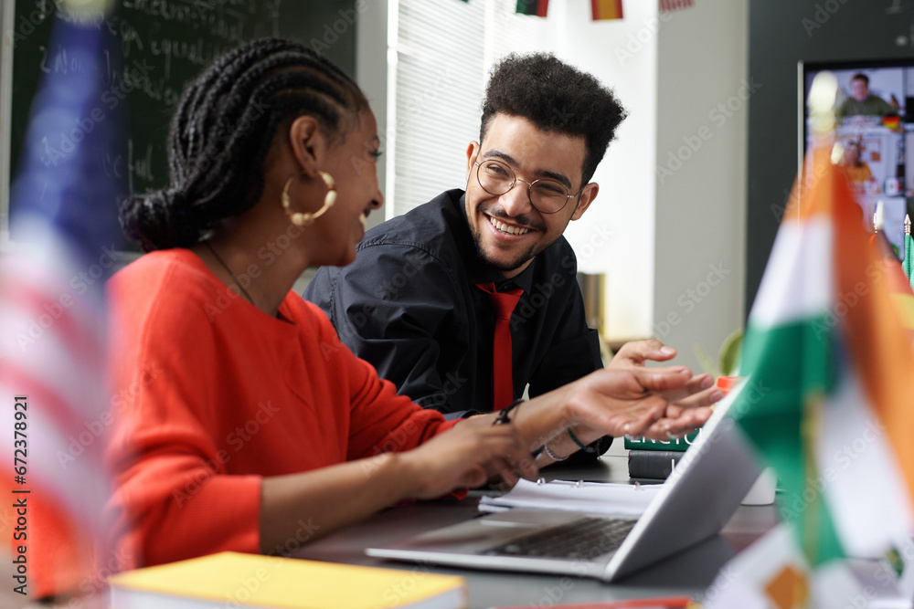 Multiethnic students discussing online work together while sitting at table with laptop Multiethnic students discussing online work together while sitting at table with laptop