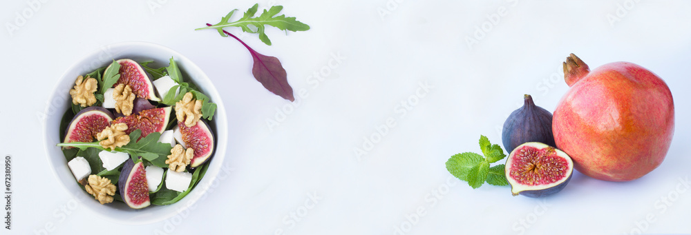 Salad with arugula, feta cheese, fig, walnut in the white bowl and fruit on the white background. Copy space.