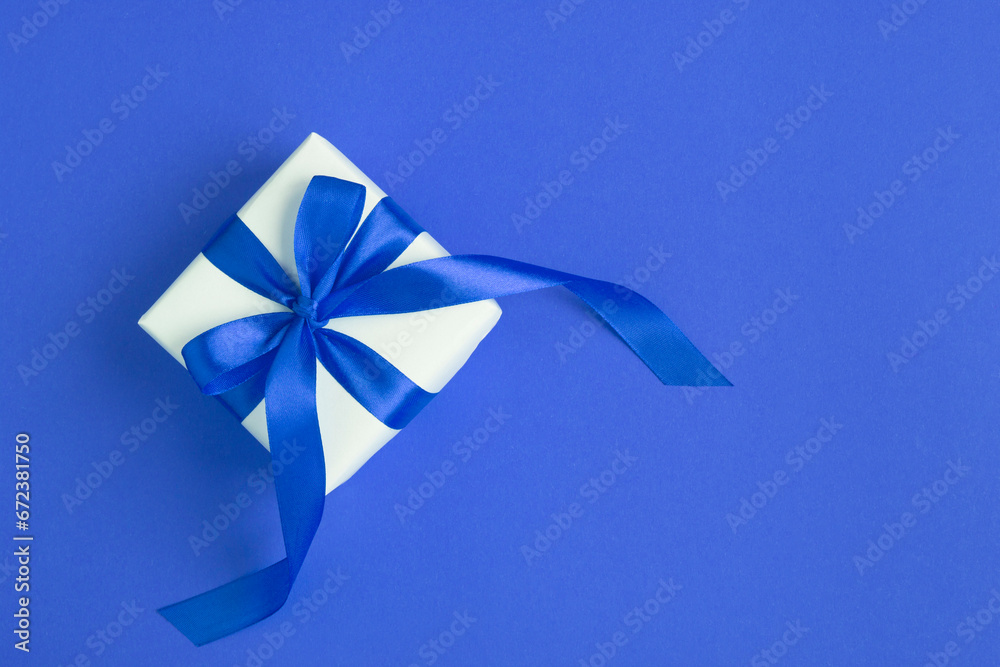 White gift box with tied blue bow on the blue background. Top view.Copy space.