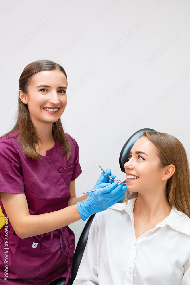 Happy young female dentist making treatment of teeth for blonde lady patient. Happy young female dentist making treatment of teeth for blonde lady patient.