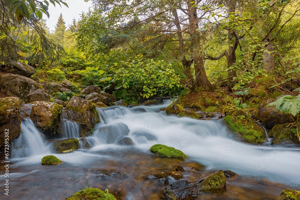 Long exposure image of a magnificent waterfall cascading over the majestic Alaskan mountain range Long exposure image of a magnificent waterfall cascading over the majestic Alaskan mountain range