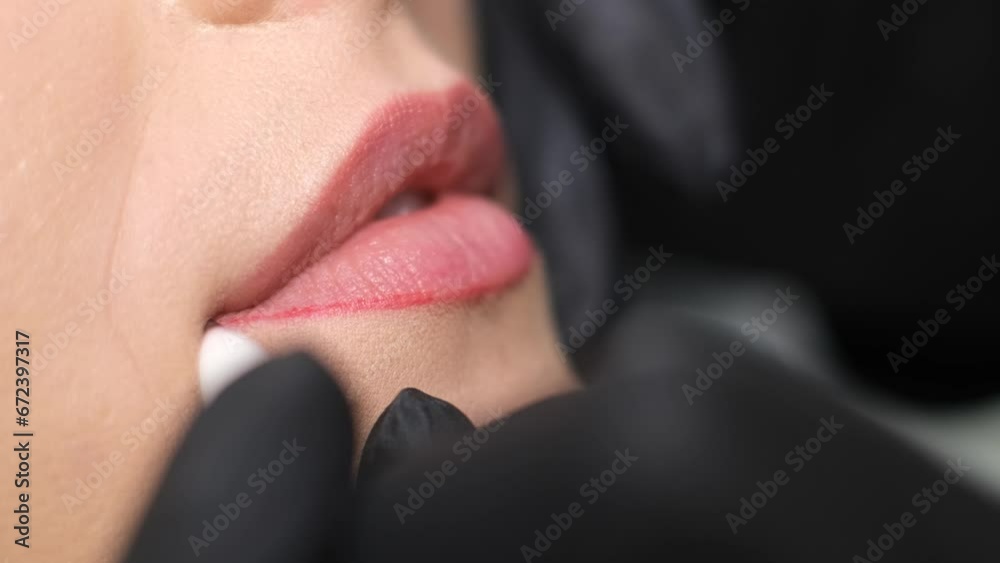 Professional permanent makeup artist and her client during lip blushing procedure. Close up.